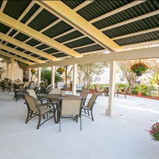 A spacious patio features several tables and chairs under a covered area, surrounded by a garden with hanging plants.