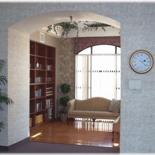 A cozy living room with a sofa, bookshelf, and clock, viewed through an arched entrance.