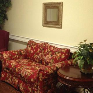 A cozy living room corner with a floral-patterned sofa, a small round table with a plant, and a framed mirror on the wall.