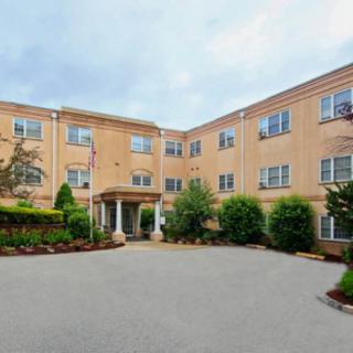 A brick apartment building with a landscaped entrance and multiple windows.