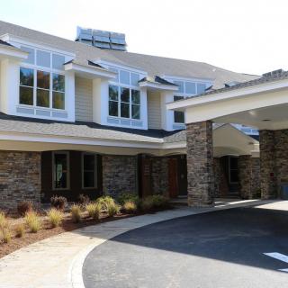 A modern residential building with stone exterior and large windows, surrounded by landscaped greenery.