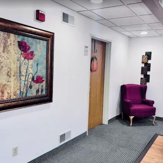 A nicely decorated office hallway featuring artwork and a purple chair.