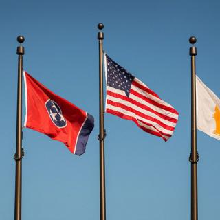 Three flags flying on flagpoles against a clear blue sky: Tennessee state flag, American flag, and an unidentified third flag.