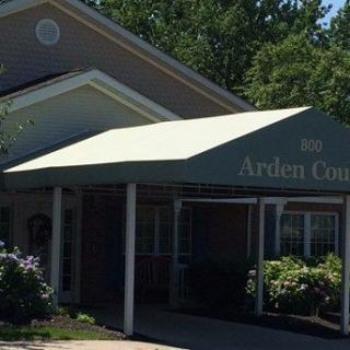 The entrance of a building with an awning, surrounded by greenery on a sunny day.