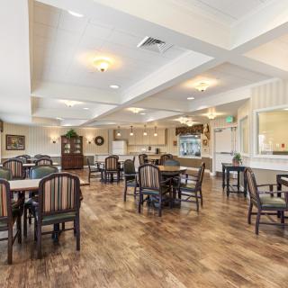 A spacious dining room with multiple tables and chairs, featuring wood flooring and ceiling lights.