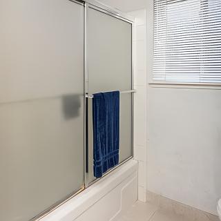 A bathroom with frosted glass shower doors and a blue towel hanging on the door, alongside window blinds.