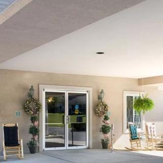 A sunny porch with seating arrangements and decorative plants near an entrance with glass doors.