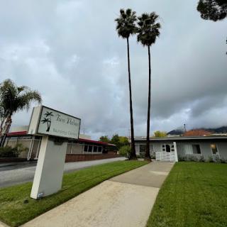 A view of a building with palm trees against a cloudy backdrop.