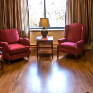 A cozy living room setting with two red armchairs, a lamp on a side table, and large windows with curtains.