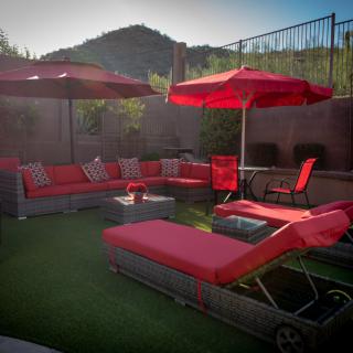 A cozy backyard patio setup featuring red lounge chairs and umbrellas with a view of the mountains in the background.