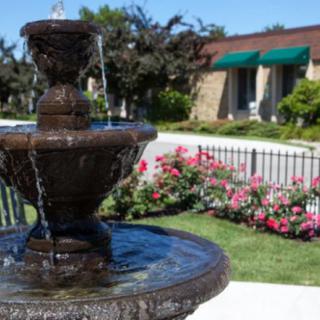 A picturesque garden featuring a fountain surrounded by blooming flowers and lush greenery.