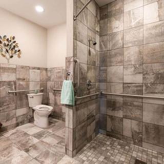 A modern bathroom with tiled walls and flooring, featuring a walk-in shower and toilet.