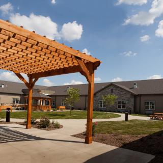 A courtyard featuring a wooden pergola and well-maintained landscaping surrounded by buildings under a clear sky.