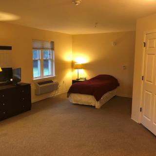 A cozy bedroom with a single bed, lamp, dresser, and window.