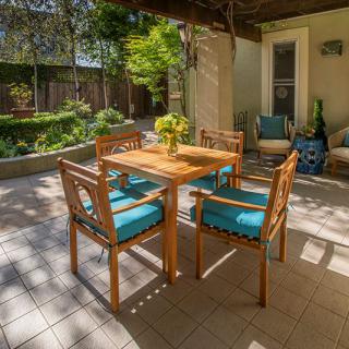A cozy outdoor patio with a wooden table and chairs, surrounded by lush greenery.