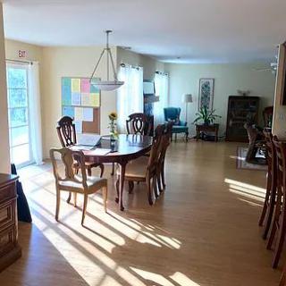 Sunlit dining room with a round table and chairs, featuring hardwood floors and large windows.