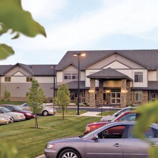 A view of a residential building with a spacious parking lot surrounded by trees.