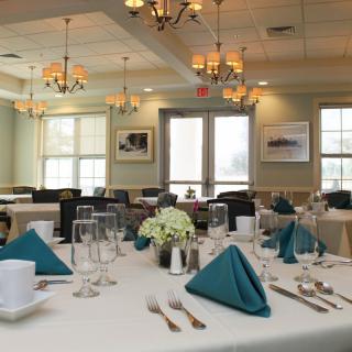 Elegantly set dining room with neatly arranged tables and teal napkins.