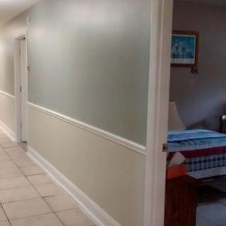 A hallway with tiled flooring leading to a bedroom, featuring soft green walls and white trim.