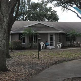 A single-story house with a front yard and chairs on the porch.