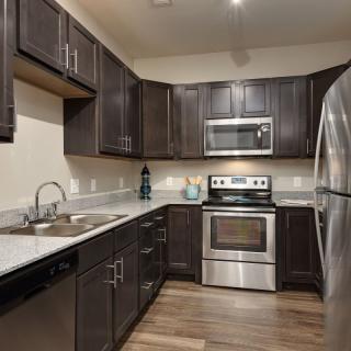 A modern kitchen with dark cabinets and stainless steel appliances.