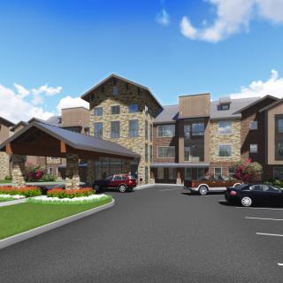 A multi-story residential building with a landscaped entrance and adjacent parking lot under a clear blue sky.