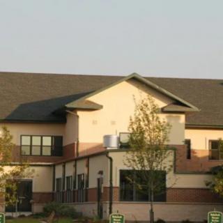 A residential building with a sloped roof and multiple windows surrounded by trees.