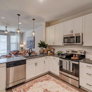 A modern kitchen with white cabinets and stainless steel appliances, featuring an island countertop and stylish pendant lighting.