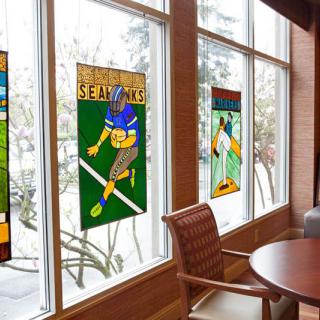 Stained glass artworks of football players displayed on large windows in an indoor seating area.