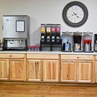 A beverage station featuring an ice machine, various drink dispensers, and a coffee setup, with wooden cabinets below and a clock on the wall.