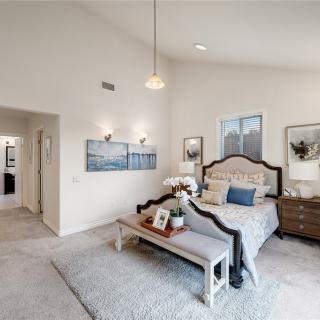 A spacious and elegantly designed bedroom featuring a large bed with decorative pillows, a bench at the foot of the bed, and stylish artwork adorning the walls.