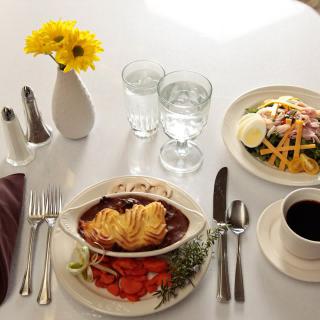 A table setting featuring a hearty meal with pasta, salad, and coffee alongside fresh yellow flowers.