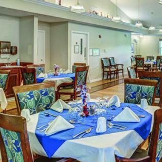 A neatly arranged dining room with tables set, featuring blue and white tablecloths and decorative napkins.
