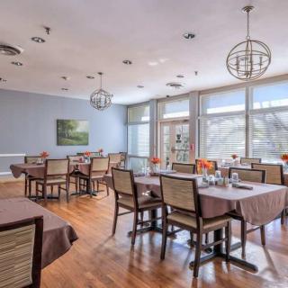 A modern restaurant dining area with neatly arranged tables and chairs, illuminated by natural light through large windows.