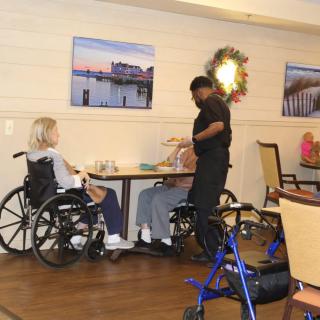 A caregiver assists elderly residents in wheelchairs at a nursing home's dining area.