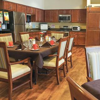 A cozy kitchen and dining area with a wooden table set for a meal, surrounded by chairs on a polished wooden floor.