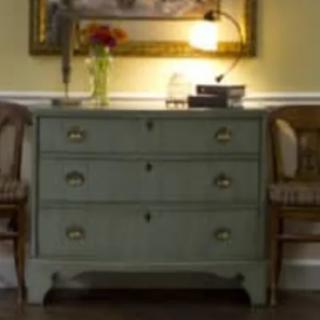 A cozy interior featuring a vintage dresser with a lamp and painting above, flanked by two wooden chairs.