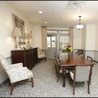 A well-furnished dining room with a long table and upholstered chairs, featuring elegant decor and soft lighting.