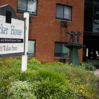 Entrance of a brick building with a sign and a statue surrounded by greenery.