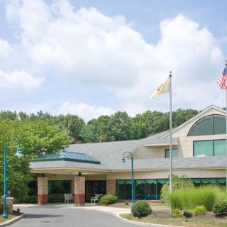 A view of a building entrance with flags flying and a driveway leading up to it, surrounded by trees under a partly cloudy sky.