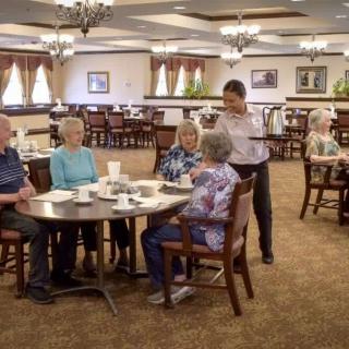 A group of seniors being served by a waiter in a spacious dining area.