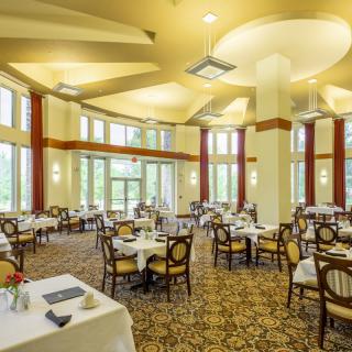A spacious dining area with multiple tables and chairs, featuring large windows and elegant lighting.