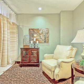 A cozy living room corner with an armchair, lamp, and cabinet adorned with artwork.