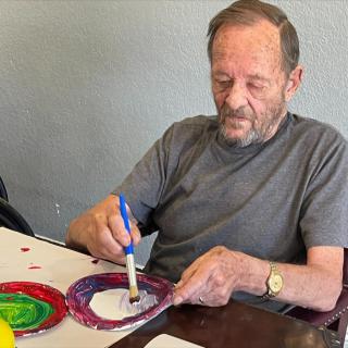 A man engaged in painting with brushes at a table, creating colorful artwork.