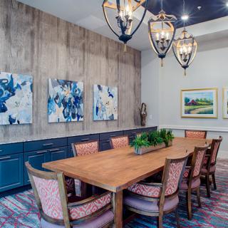 A stylish dining room featuring a long wooden table, elegant chairs, and modern chandeliers, complemented by artwork on the walls.