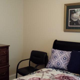 A cozy bedroom featuring a bed with decorative pillows, a wooden dresser, and a framed picture on the wall.
