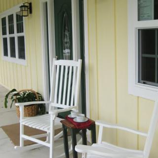 Inviting front porch with white rocking chairs and a small table against a yellow house exterior.