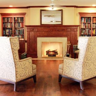 A cozy living room with a fireplace, surrounded by bookshelves and comfortable chairs.