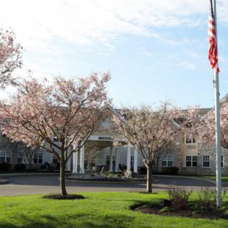 A well-maintained building with a landscaped entrance and flowering trees, featuring a flagpole in the foreground.