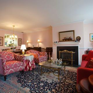 A cozy living room featuring traditional decor with sofas and armchairs arranged around a fireplace, complemented by a patterned rug and ambient lighting.